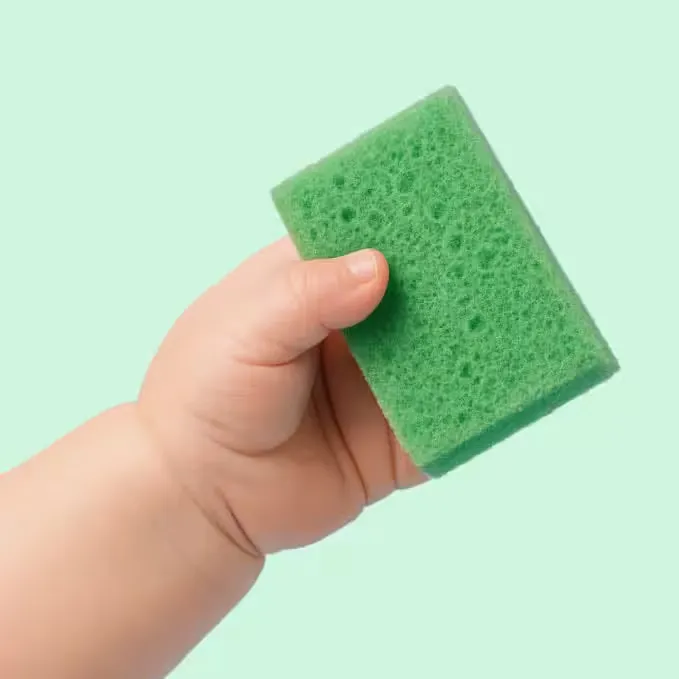 Mână de bebeluș lângă un burete de bucătărie - cantitatea lunară de microplastic la copii